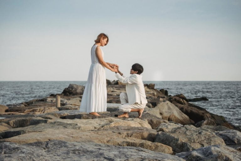 a man and woman holding hands on a rocky beach